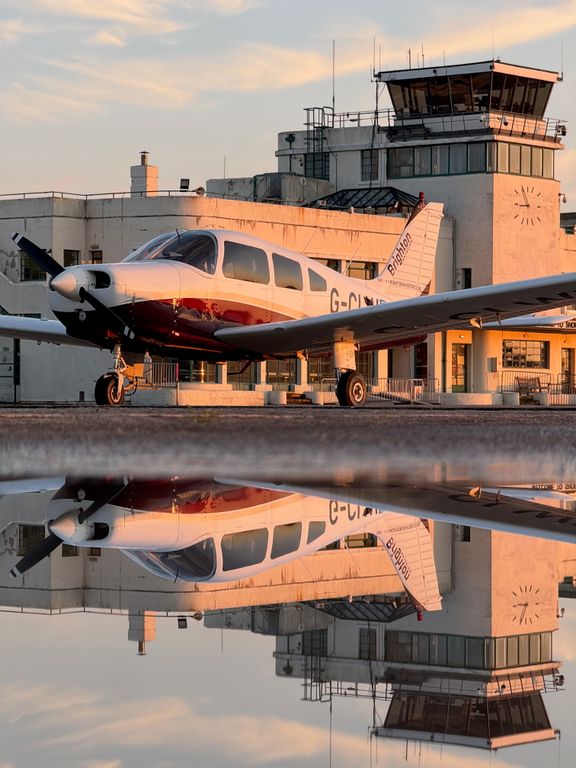 A reflective picture of a STAR Flight Training PA28, G-CLWD, in front of the terminal building at Brighton City Airport (SHOREHAM)