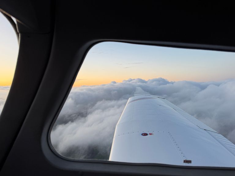 A view in flight out of the passenger window looking over the wing above cloud in a Piper PA28