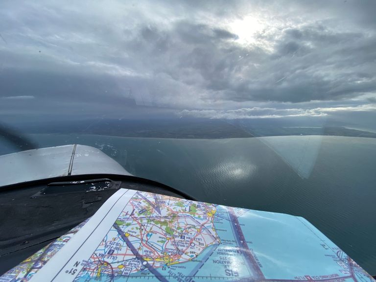 View from the cockpit of a Piper PA-28 with a VFR flying chart on the dashboard over the sea